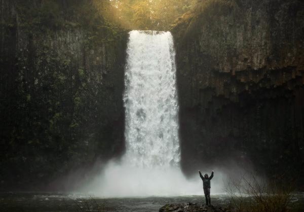 Happy Man Standing in Front of Waterfall because of Negative Ions